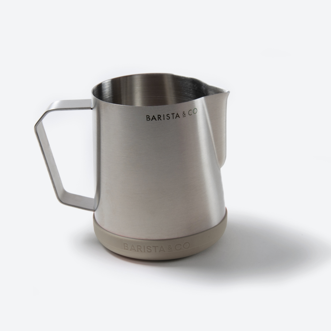 A brushed stainless steel milk pitcher with a matte-finish base and the BARISTA & CO logo printed on both the side and the base, set against a clean white background.