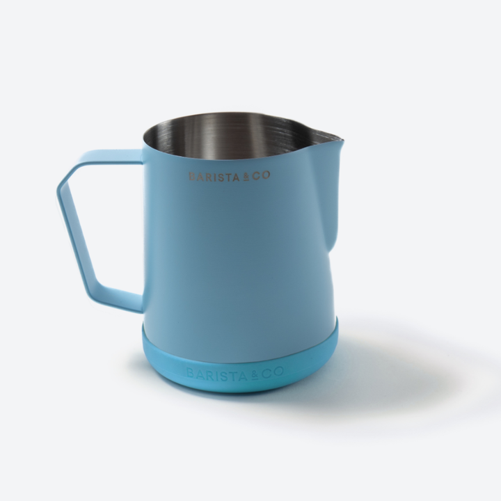 A light blue stainless steel milk pitcher with a matching blue base and handle, featuring the BARISTA & CO logo, on a clean white background.