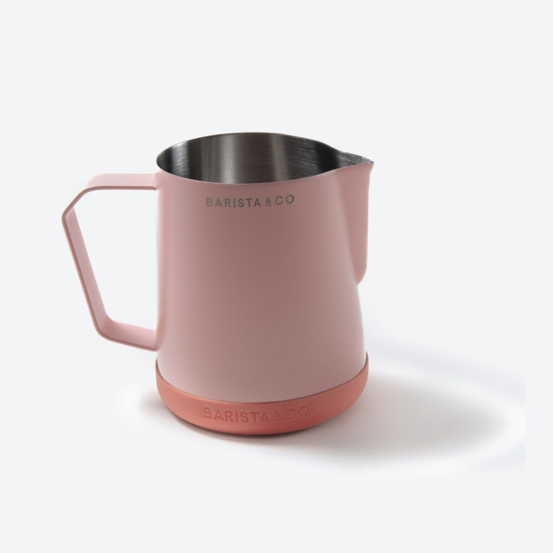 A Barista & Co. stainless steel milk pitcher with a matte dusty pink body, handle, and base, shown on a clean white background.