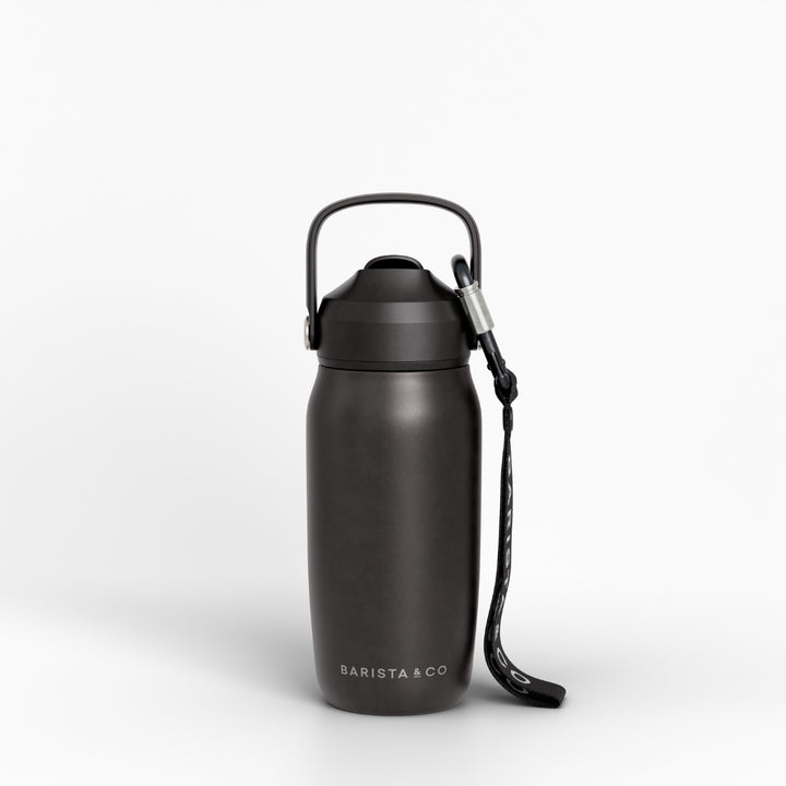 A matte black insulated water bottle with a carrying loop and wrist strap, featuring the BARISTA & CO logo near the base, set against a clean white background.