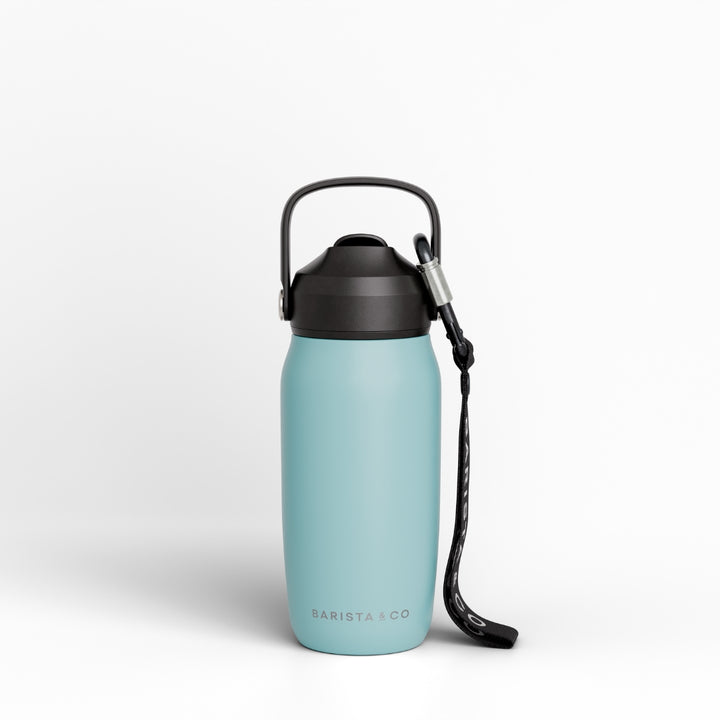 A light blue insulated water bottle with a black lid, carrying loop, and black wrist strap, shown on a clean white background. The brand name 'BARISTA CO' is printed near the bottom.