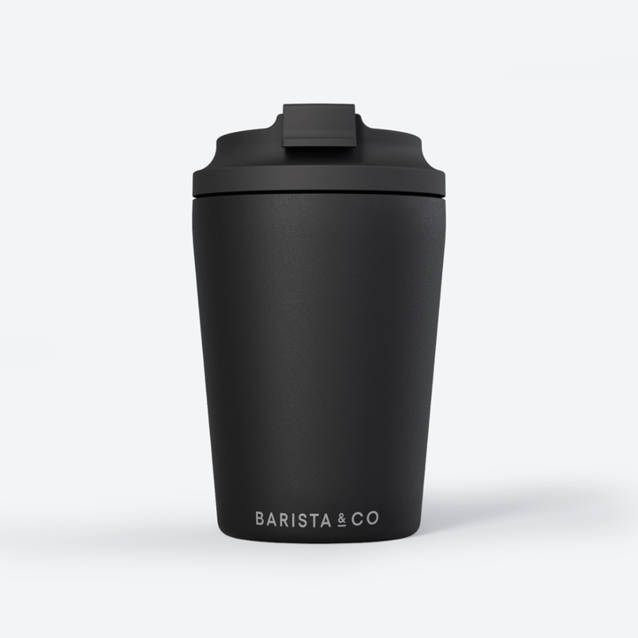 A matte black travel tumbler with a matching black lid and the white text 'BARISTA & CO' printed near the bottom, shown on a clean white background.