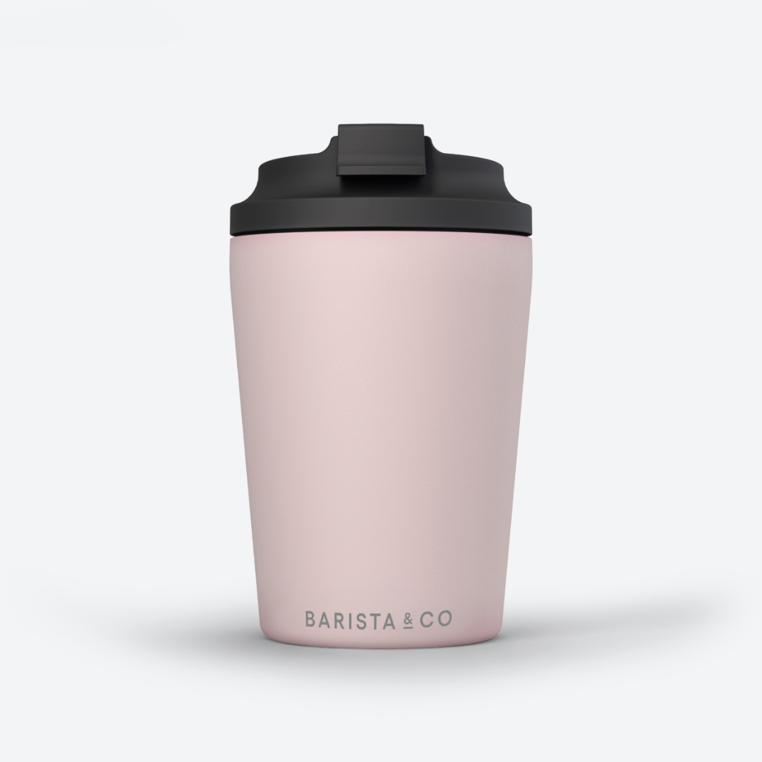 A light pink travel tumbler with a black lid, featuring the 'BARISTA & CO' logo printed in gray near the bottom, set against a clean white background.