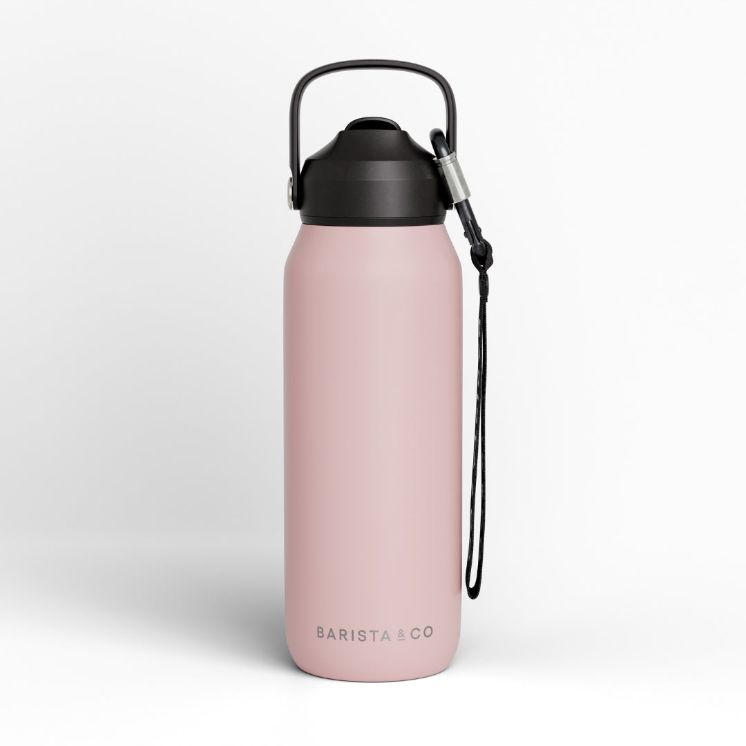 A matte pink insulated water bottle with a black lid, carrying loop, and wrist strap, shown on a clean light gray background. The brand name 'BARISTA & CO' is printed near the bottom.