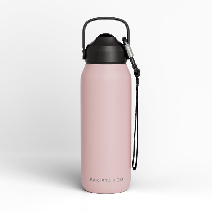 A matte pink insulated water bottle with a black lid, carrying loop, and wrist strap, shown on a clean light gray background. The brand name 'BARISTA & CO' is printed near the bottom.