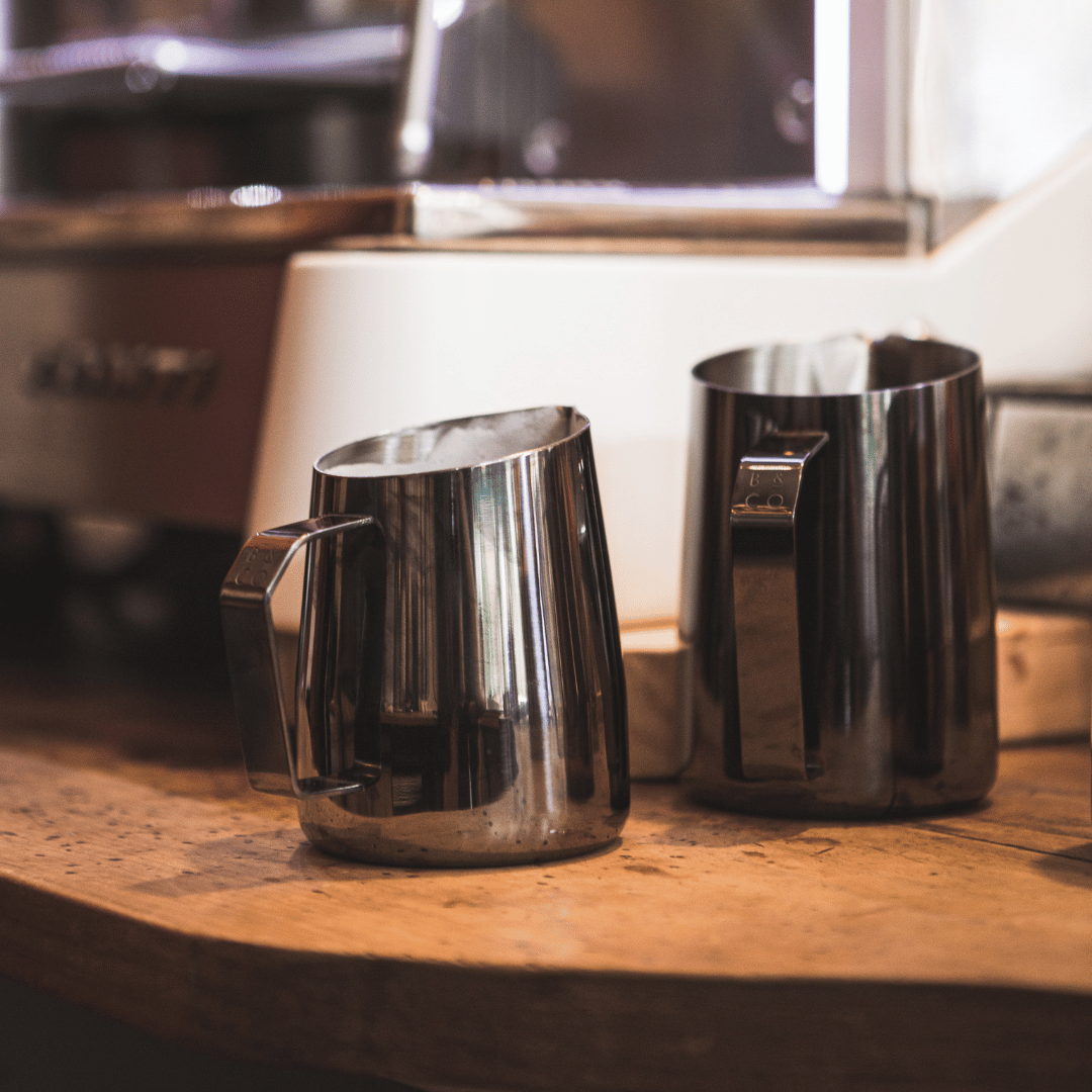 pair of black milk frothing jugs in a coffee shop